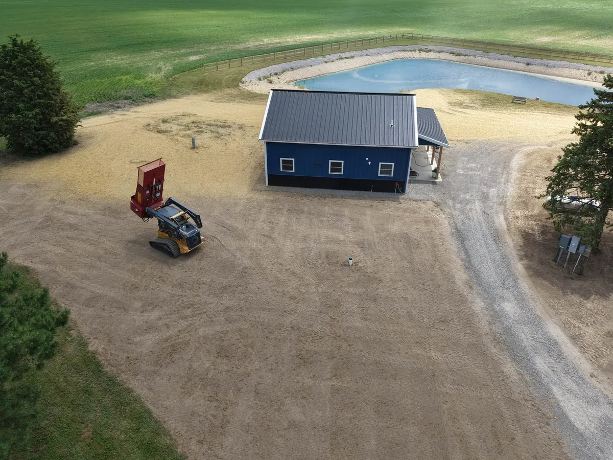 Drone view of a new pond beside a blue pole barn on freshly graded ground